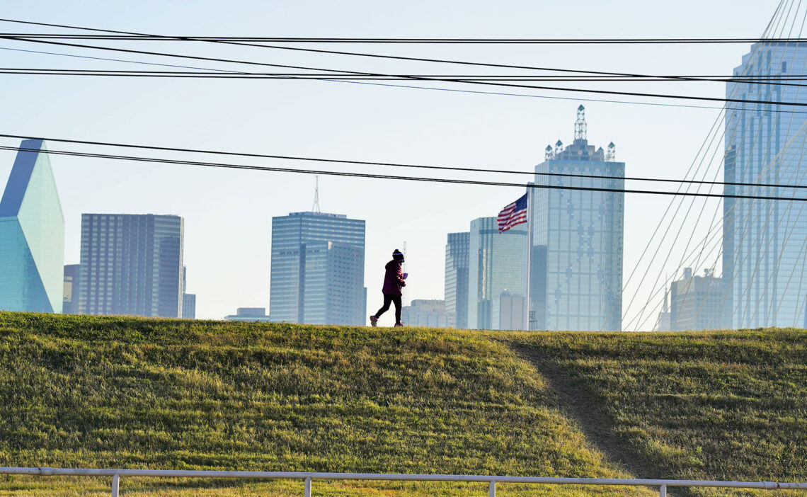 A woman jogs along the Trinity River trail in Dallas, with downtown in the background.